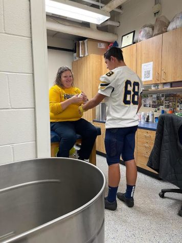 Tina Hackley helps football player Niko Leon (10) get wrapped for the Hylanders upcoming football game. 